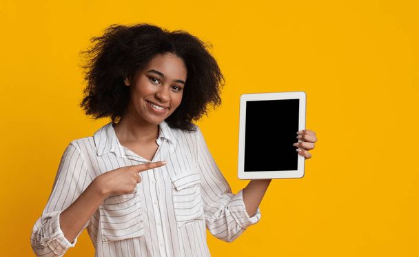 Mujer sonriente sosteniendo y señalando la tableta digital con pantalla negra
 - Foto, imagen