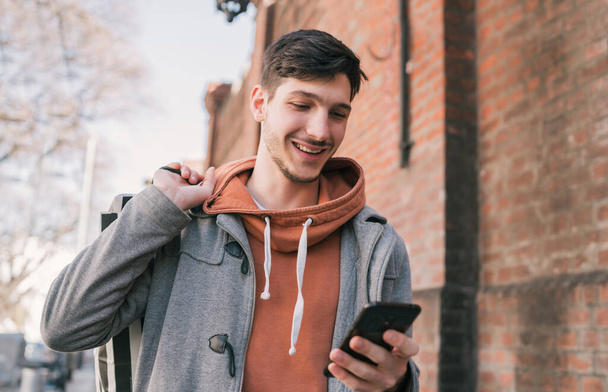 Egy portré fiatal jóképű férfiról, aki az utcán sétál, bevásárlószatyrokkal a kezében és használja a mobilját. Városi, üzletkoncepció. - Fotó, kép
