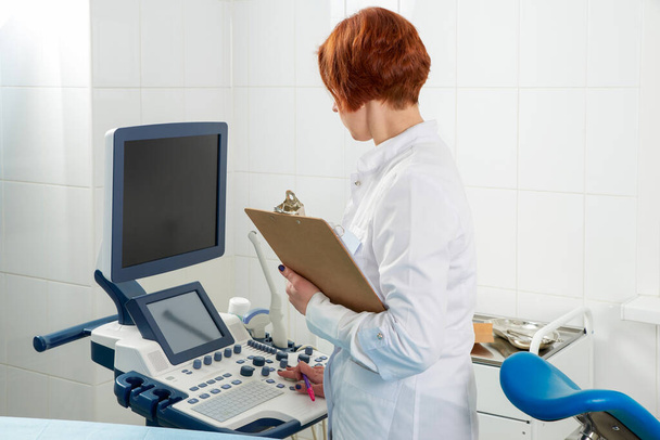 Klinikteki modern ultrason makinesinin yanında panosu olan profesyonel bir doktor. - Fotoğraf, Görsel