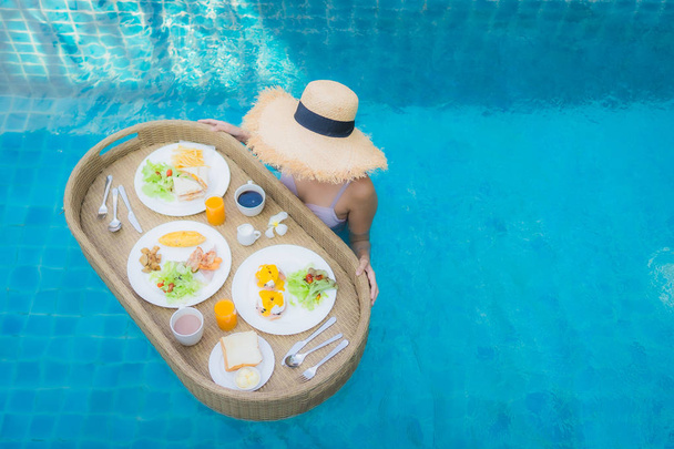 Portrét mladé asijské ženy šťastný úsměv těšit s plovoucí snídaně tác v bazénu v hotelovém resortu - Fotografie, Obrázek