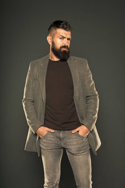 The beard stays in fashion. Fashion guy. Fashion model keeping arms in pockets on grey background. Bearded man with fashion look. Brutal hipster with beard and mustache hair in casual style - Foto, afbeelding