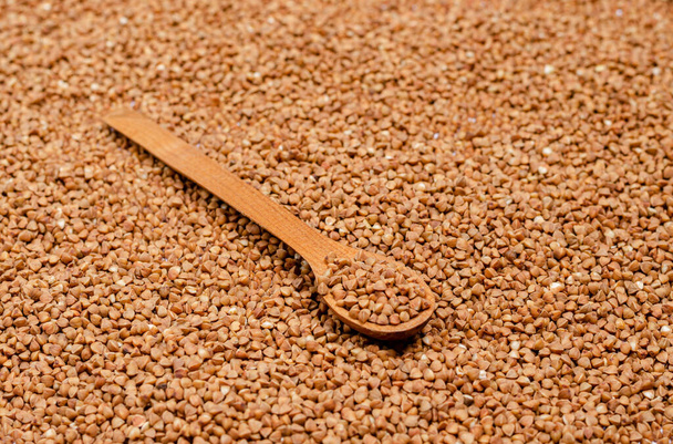 Dry groats for vegans in a wooden spoon on a background of buckwheat. Healthy foods high in protein and carbohydrates. View from above. Horizontal orientation. - Foto, afbeelding