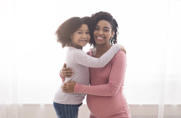 Afeição familiar. Sorrindo preto menina abraçando com a mãe em casa
 - Foto, Imagem