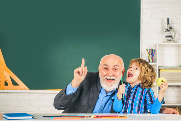 Pupil and Teacher in classroom. Grandfather and son having fun together. Mature man teacher and pupil on balckboard background. - Foto, Imagem