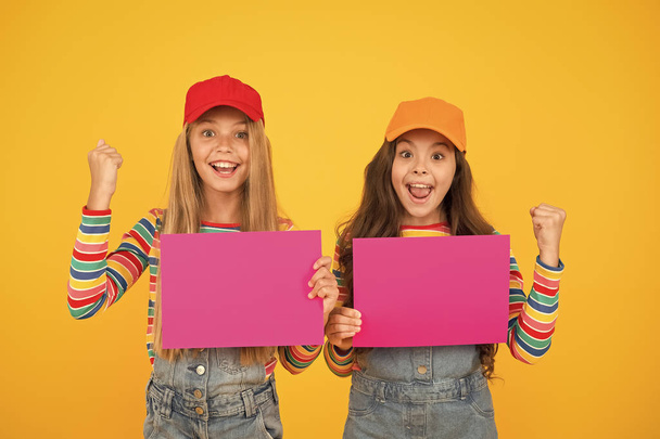 Your advertising wins. Happy small children showing pink paper sheets for advertising on yellow background. Little girl advertising product or event. Winning advertising solutions for you, copy space - Valokuva, kuva