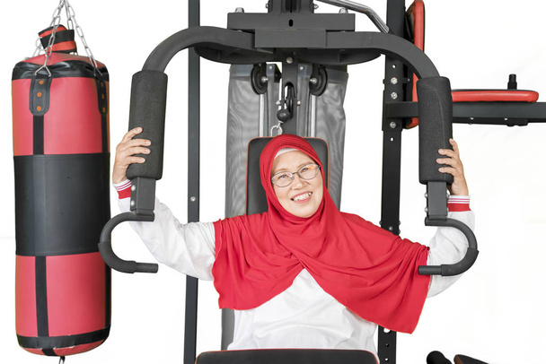 Portret van aantrekkelijke moslim senior vrouw lachend naar de camera terwijl ze traint op een fitnessapparaat - Foto, afbeelding