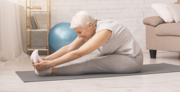 Active senior woman doing stretching exercises at home - Fotoğraf, Görsel
