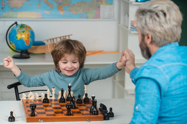 Young kid boy playing chess with father and having fun. Educational games. Handsome father and son are playing chess while spending time together. - Foto, imagen