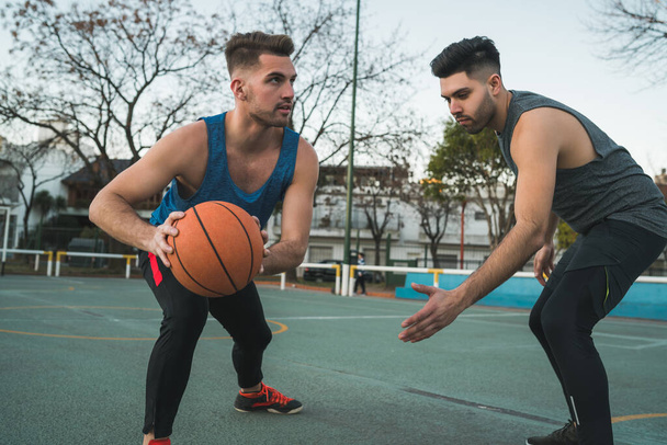 Portrait of two young friends playing basketball and having fun on court outdoors. Sports concept. - Foto, afbeelding