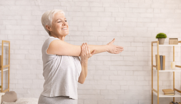 Positive senior lady warming up her hands at home - Photo, Image
