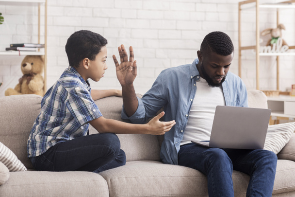 Pieni Afro poika pyytää huomiota isältään kiireinen kannettavan tietokoneen kanssa
 - Valokuva, kuva