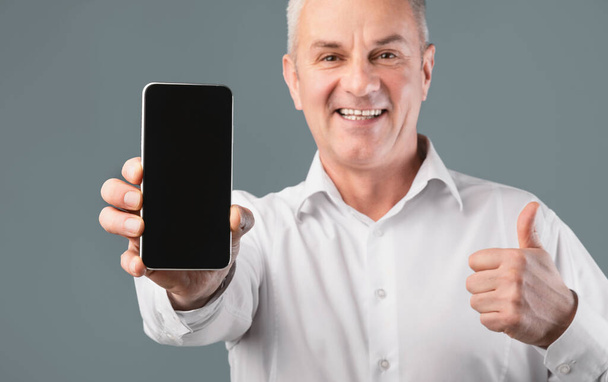 Hymyilevä mies näyttää matkapuhelimen tyhjällä näytöllä
 - Valokuva, kuva