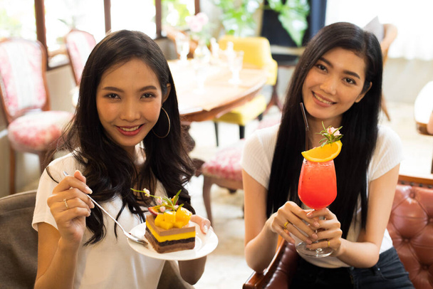 Két ázsiai nővérek, hogy fotó és íze finom édes torta és gyümölcslé, A legjobb barátok mosolyognak együtt gyönyörű design torta és smoothies frissítő butik étterem kávézó utazás közben - Fotó, kép