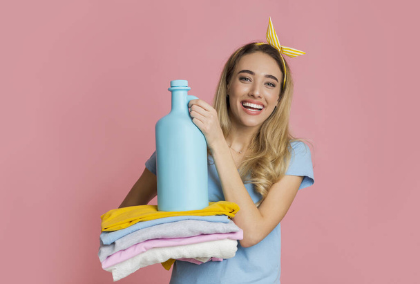 Menina sorridente detém roupas limpas e amaciador de tecido
 - Foto, Imagem