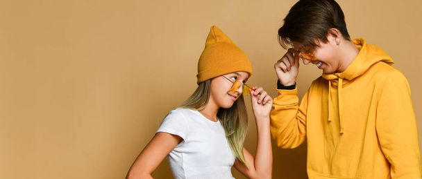 Young teens boy and girl in comfortable clothing and hats standing and looking at each other from sunglasses - Photo, Image