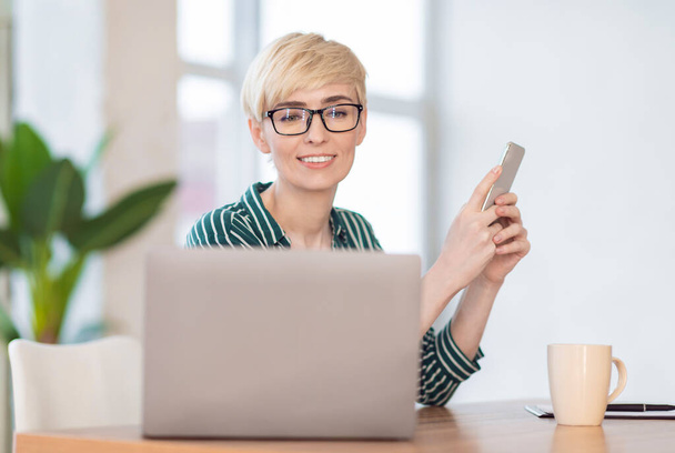 Весела бізнес-леді використовуючи мобільний телефон додаток сидячи в офісі
 - Фото, зображення
