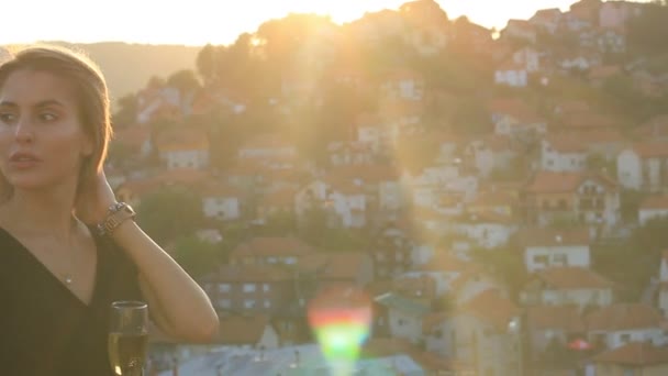 Atraktivní žena se sklenkou šampaňského na terase na zlaté hodině slunečního podsvícení - Záběry, video