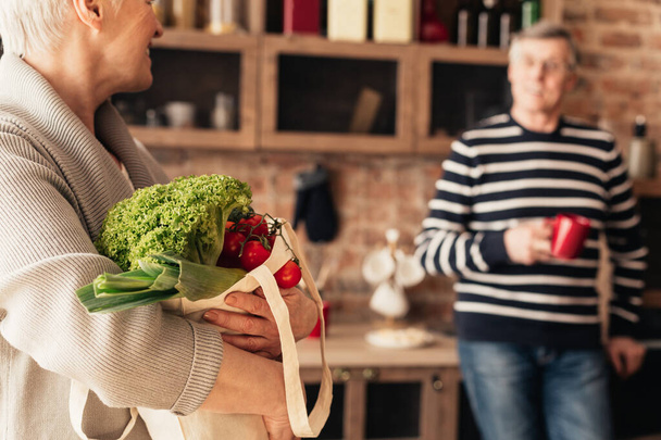 Casal de idosos desembalando eco bag com legumes orgânicos na cozinha
 - Foto, Imagem