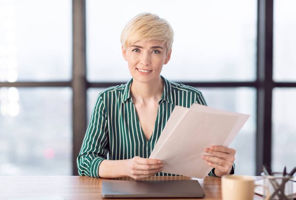 Femme d'affaires tenant des papiers et des documents souriant assis dans le bureau
 - Photo, image