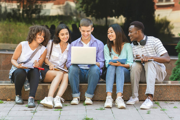 Groupe d'étudiants universitaires utilisant un ordinateur portable en plein air, se préparer pour les cours ensemble
 - Photo, image