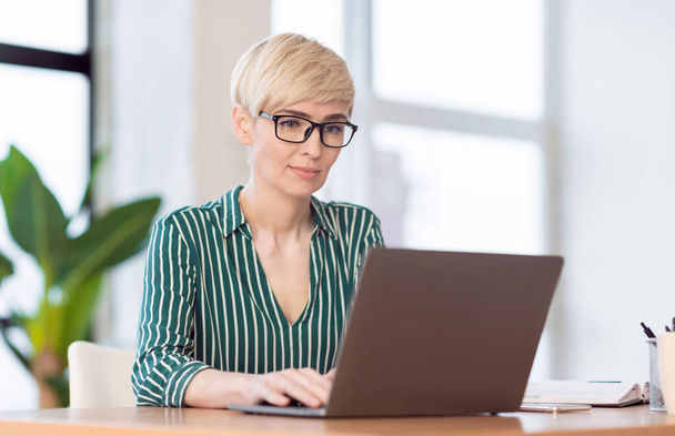 офіс менеджер леді працює на ноутбук сидячи на робочому місці в приміщенні
 - Фото, зображення