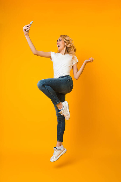 Overjoyed woman jumping and taking selfie on phone - Fotoğraf, Görsel