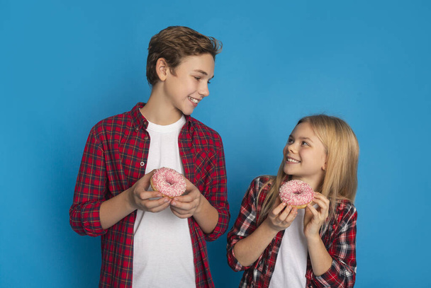 Братья и сёстры. Happy Little Brother and Sister Holding Sweet Tasty Donuts
 - Фото, изображение
