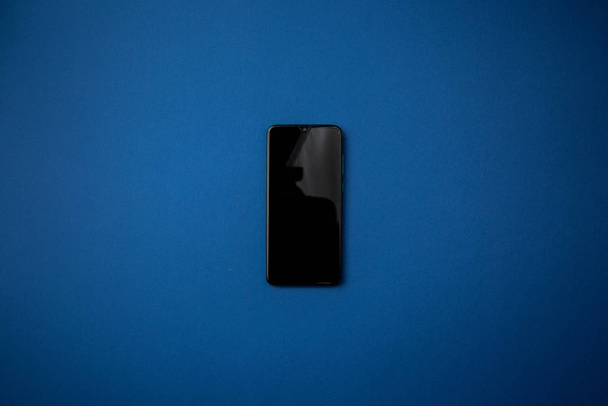 Black smartphone on a blue background. - Zdjęcie, obraz