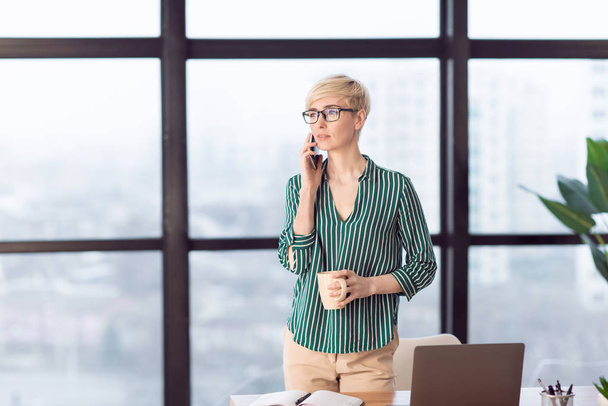 Serious Businesswoman Talking On Cellphone Standing Near Window In Office - Zdjęcie, obraz