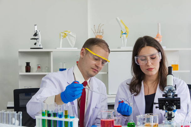 female and male scientist ware safety glasses are doing dip chemical to beaker in laboratory - Zdjęcie, obraz