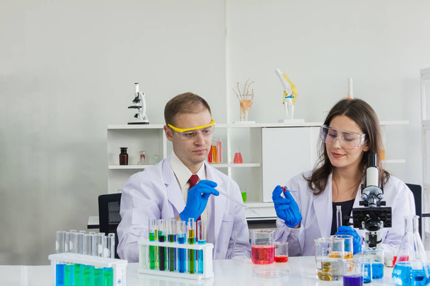 occhiali di sicurezza scientifici femminili e maschili stanno facendo immersione chimica a becher in laboratorio
 - Foto, immagini