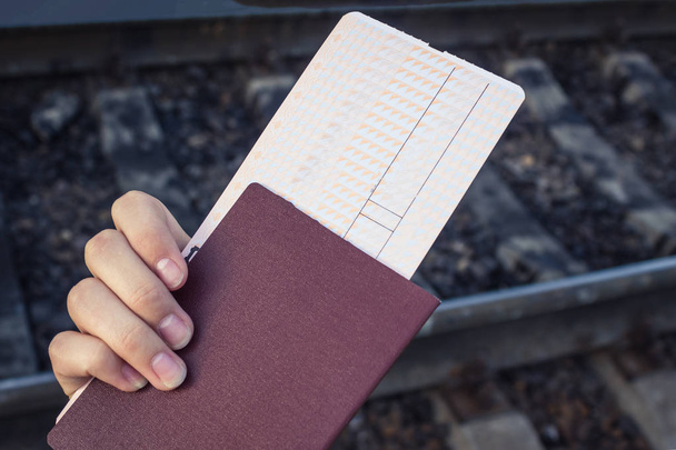 In his hand is a passport and a ticket. A trip, the upcoming road. In the background, dark rails. - Fotoğraf, Görsel