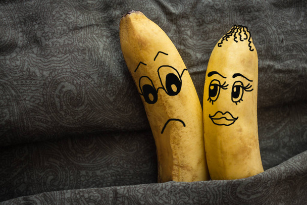 One banana, a woman, sticks to another banana in bed. Strong inclination, passion, desire for sex, flirtation. Dark background. The picture is made by the author. - Photo, Image