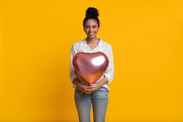 Beautiful afro girl with heart shaped air balloon on yellow background - Fotografie, Obrázek