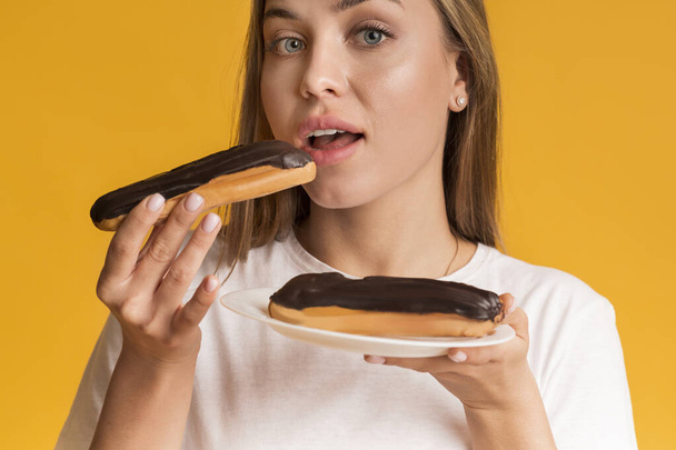 Nuori nainen syö Eclairs suklaata Cream ja katsot kameraa
 - Valokuva, kuva