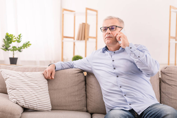 Serious mature man talking on mobile phone at home - Fotó, kép