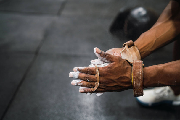 Portrait of fitness young man rubbing hands with chalk magnesium powder, preparing for workout in crossfit gym. Sport and healthy lifestyle concept. - Фото, изображение