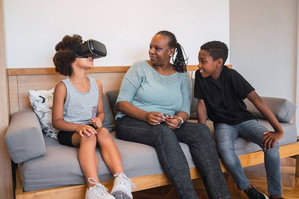 Portrait of African American grandmother and grandchildren playing together with VR glasses at home. Family and technology concept. - 写真・画像
