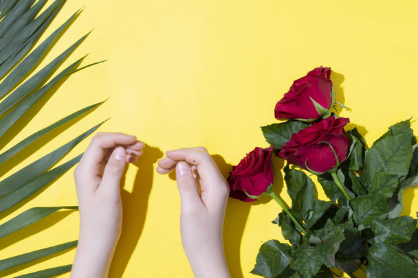 Three Red roses, kids hands and fern leaves on yellow paper. Copy space for woman day or valentines - Foto, Imagem