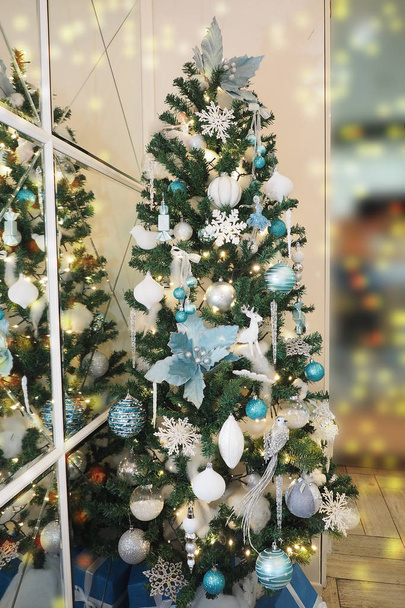 künstlichen Baum mit Spielzeug in weißen und blauen Tönen in der Nähe der Spiegelwand dekoriert, Bokeh-Lichter. verschwommener Hintergrund - Foto, Bild