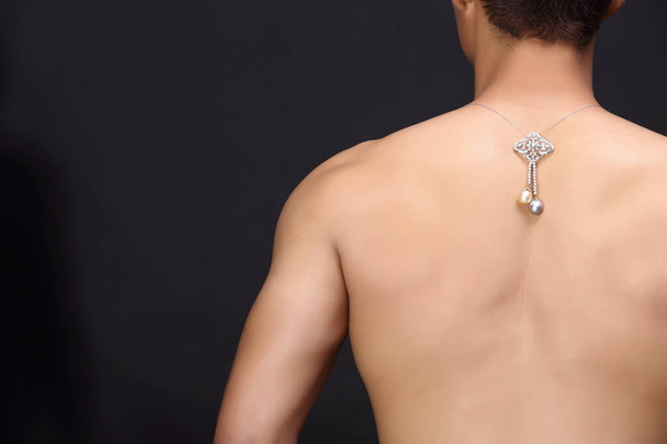Joyas, joyas, diamantes, pedante de oro cuelgan sobre la espalda muscular del modelo masculino, fondo oscuro
 - Foto, imagen