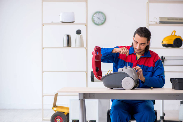 Young male contractor repairing vacuum cleaner at workshop - Photo, Image