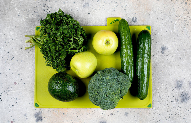 Terveellinen vegaani ruoka ruokavalio käsite. Vihreät vihannekset ja hedelmät vihreällä leikkuulaudalla betonipöydän taustalla. Ylänäkymä, tasainen. Ruoanlaitto käsite
. - Valokuva, kuva