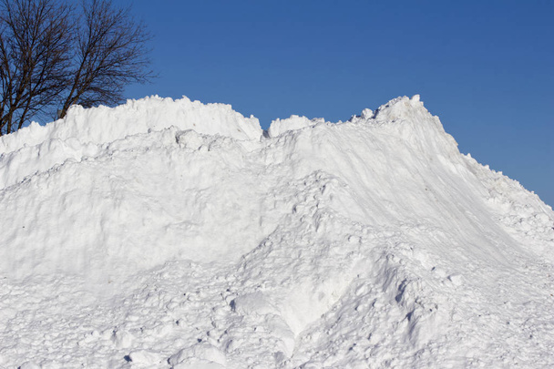 Landscape texture view of a very large pile of shoveled snow, with blue sky background and copy space - Photo, Image