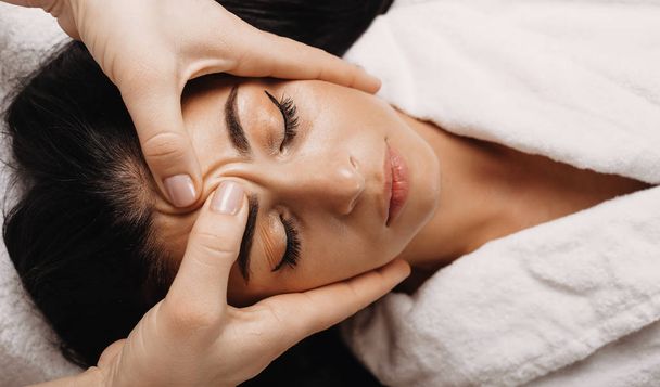 Белая девушка с черными волосами, которая спит во время массажа лица в спа
 - Фото, изображение