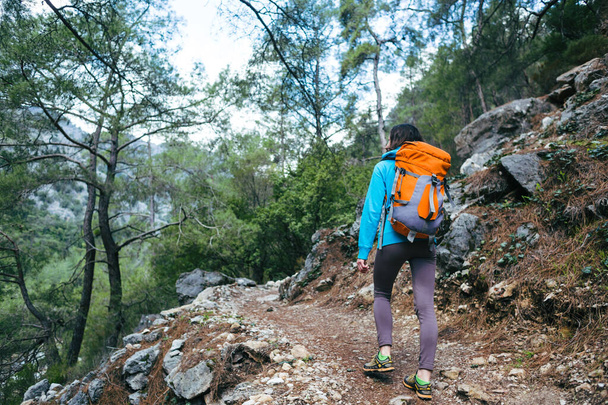 Μια γυναίκα ταξιδεύει μόνη σε γραφικά μέρη. Ένα κορίτσι με σακίδιο ακολουθεί ένα μονοπάτι στο βουνό. Μια γυναίκα περπατά μόνη στο δάσος.. - Φωτογραφία, εικόνα