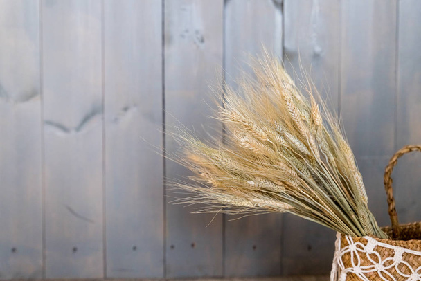 Elegant Bush of dry grass in basket decorated at cafe against wooden wall background.bundle of ears.Golden ears of wheat in vase.home decoration.Natural eco home decor with wild rye bouquet. - Fotografie, Obrázek