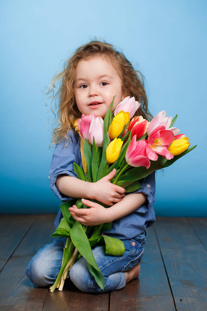 Frühlingsporträt eines lächelnden kleinen Mädchens mit roten lockigen Haaren, das einen Strauß mehrfarbiger Tulpen als Geschenk hält, isoliert auf hellgrünem Hintergrund im Studio. Ein nettes kleines Mädchen mit einem Strauß Tulpen, im Frühling im Atelier. - Foto, Bild