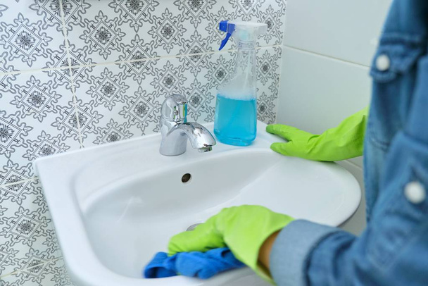 Frau putzt und poliert Waschbecken und Wasserhahn im Badezimmer - Foto, Bild