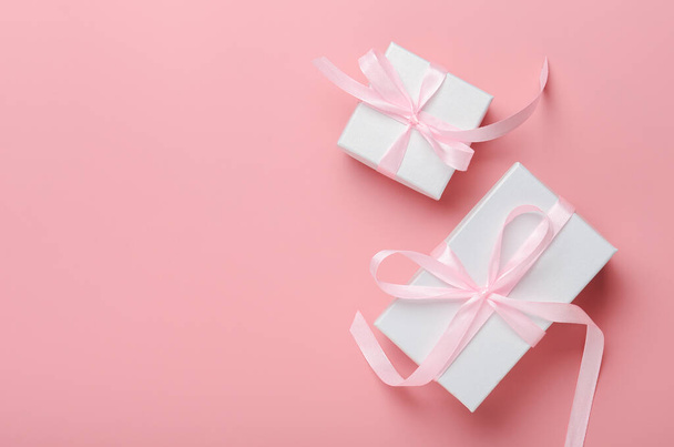 ピンクのリボン付きのピンクの背景に白いギフトボックス。誕生日プレゼント、女性の日またはクリスマス。トップビュー、保存スペース、フラットレイアウト. - 写真・画像